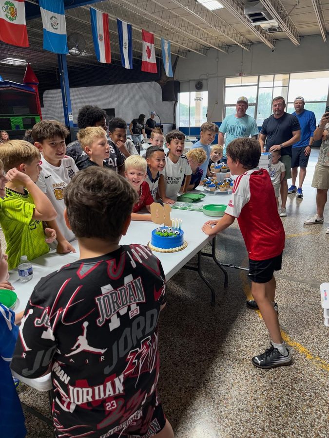 Birthday Party at StudioX Soccer Arena - kids gathered around a soccer birthday cake with bounce house in the background